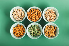 Six bowls of different types of nuts on a green background