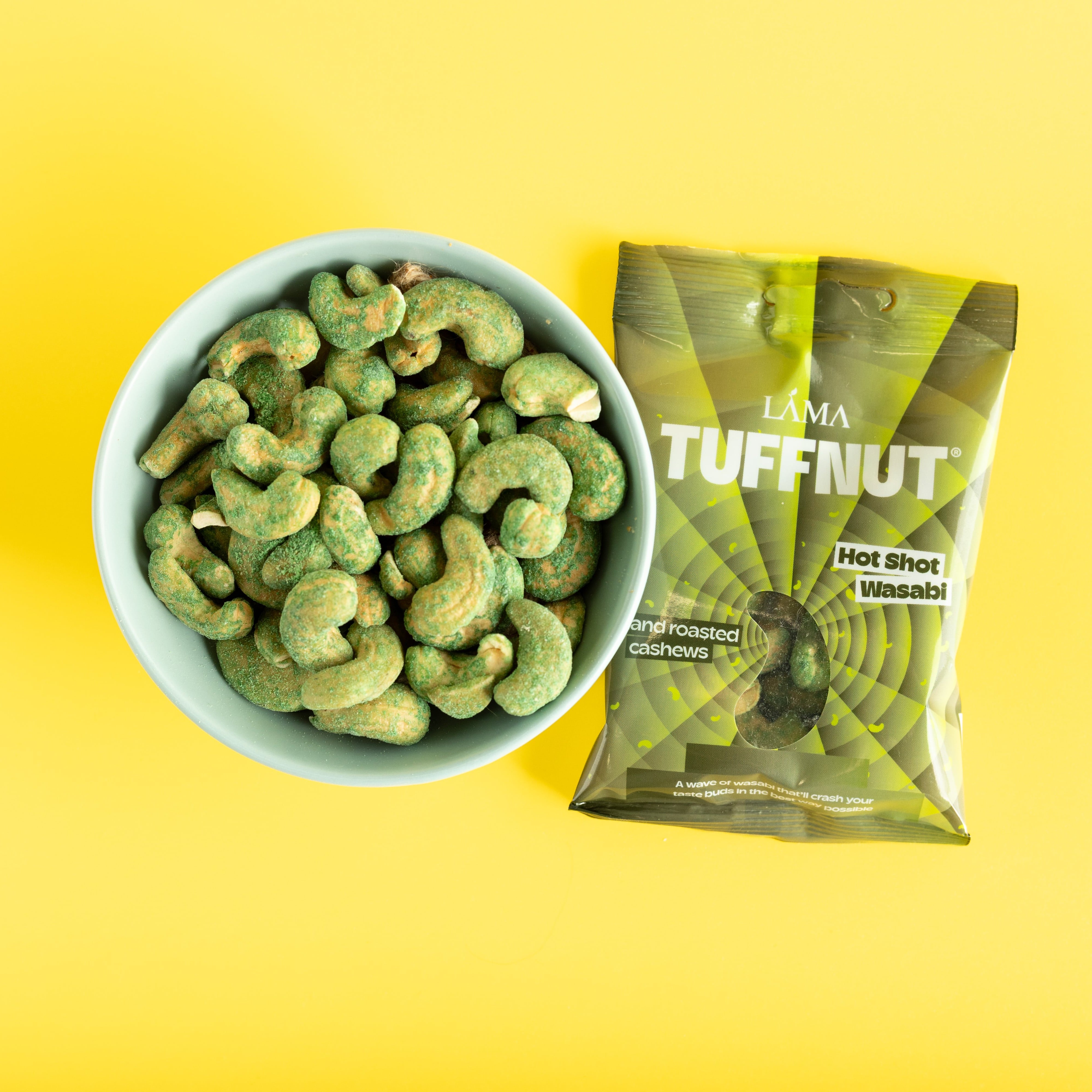 Bowl of wasabi cashews next to a package of Tuffnut on a yellow background