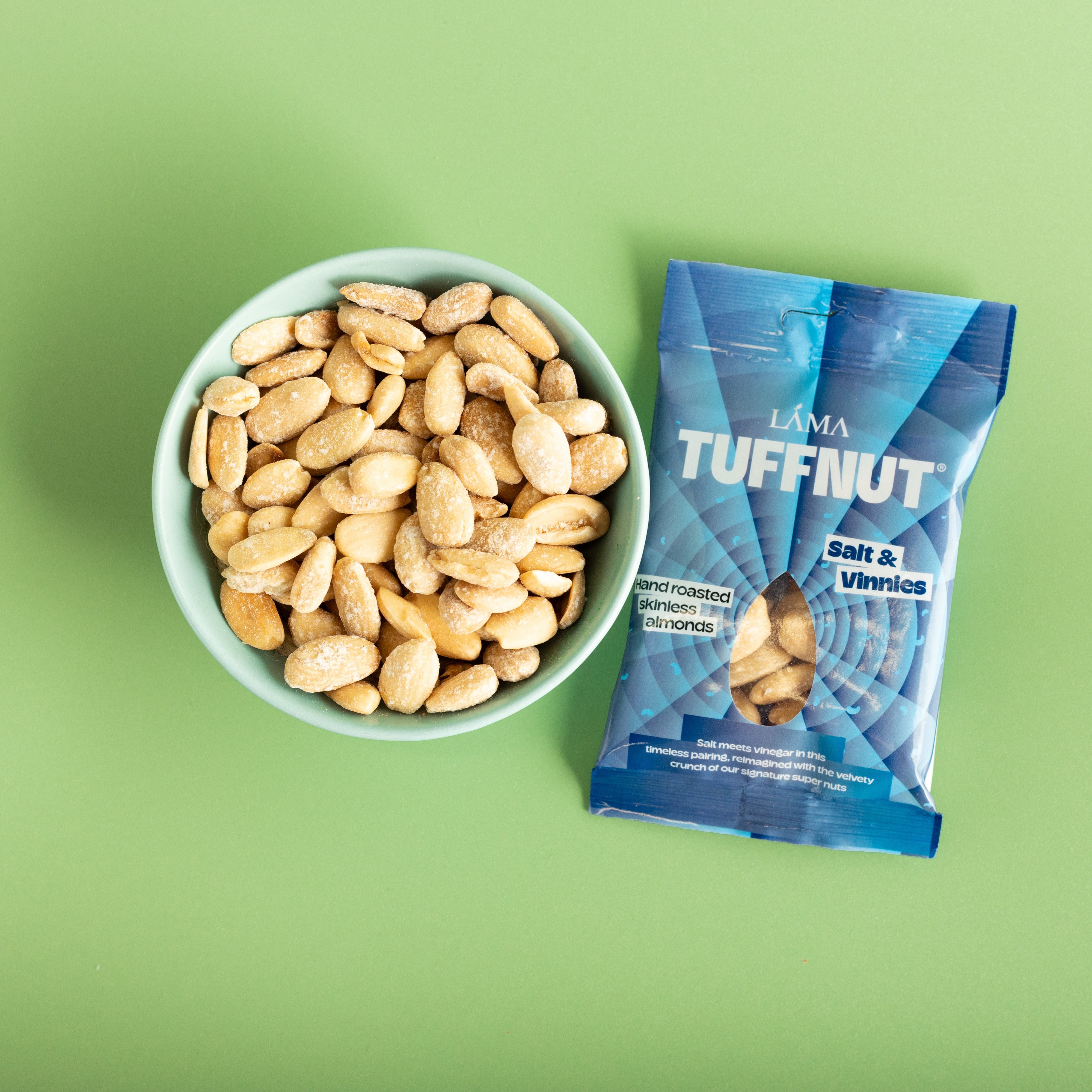 Bowl of skinless almonds next to a blue package labeled 'Tuffnut' on a green background.