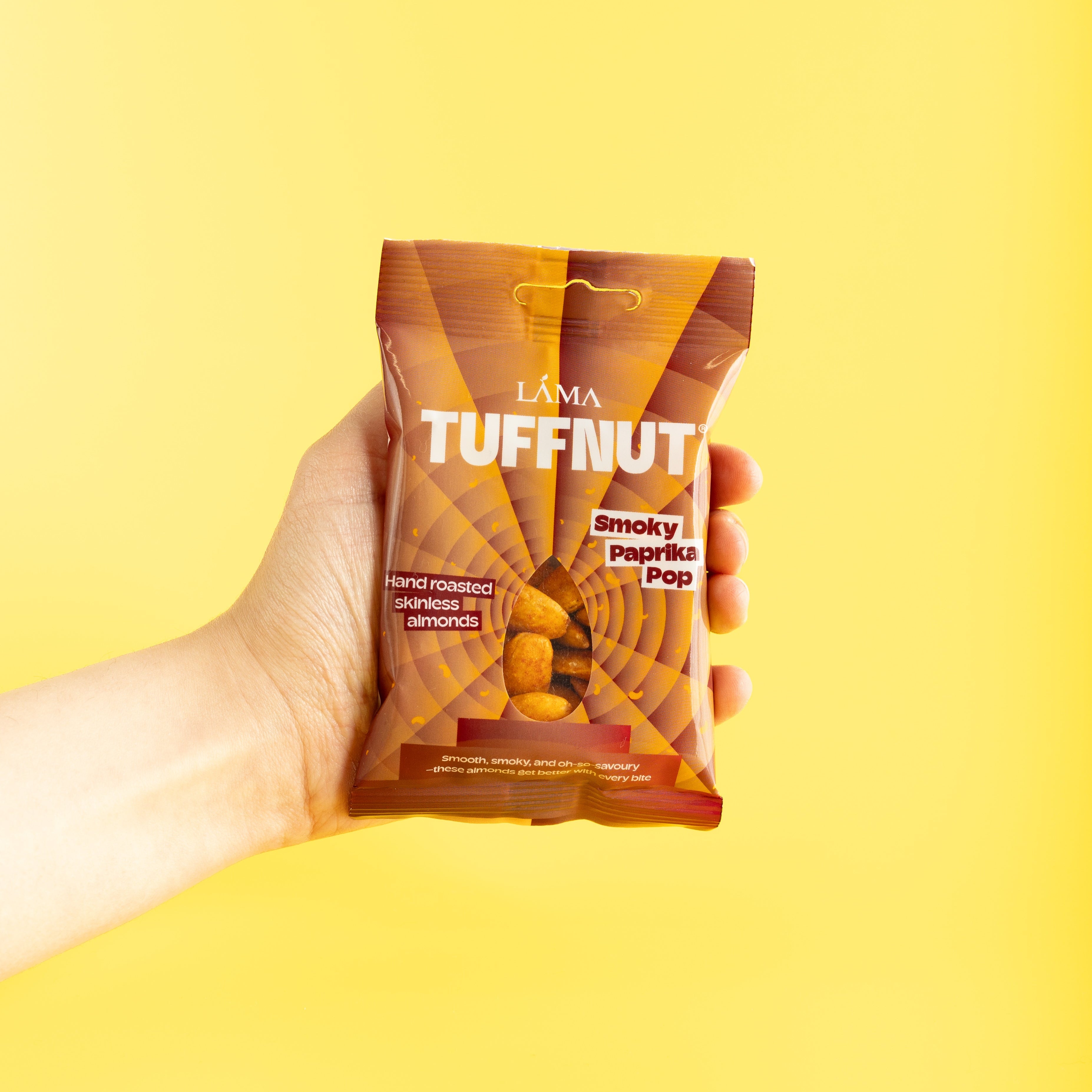 Hand holding a Tuffnut smokey paprika pop snack package against a yellow background
