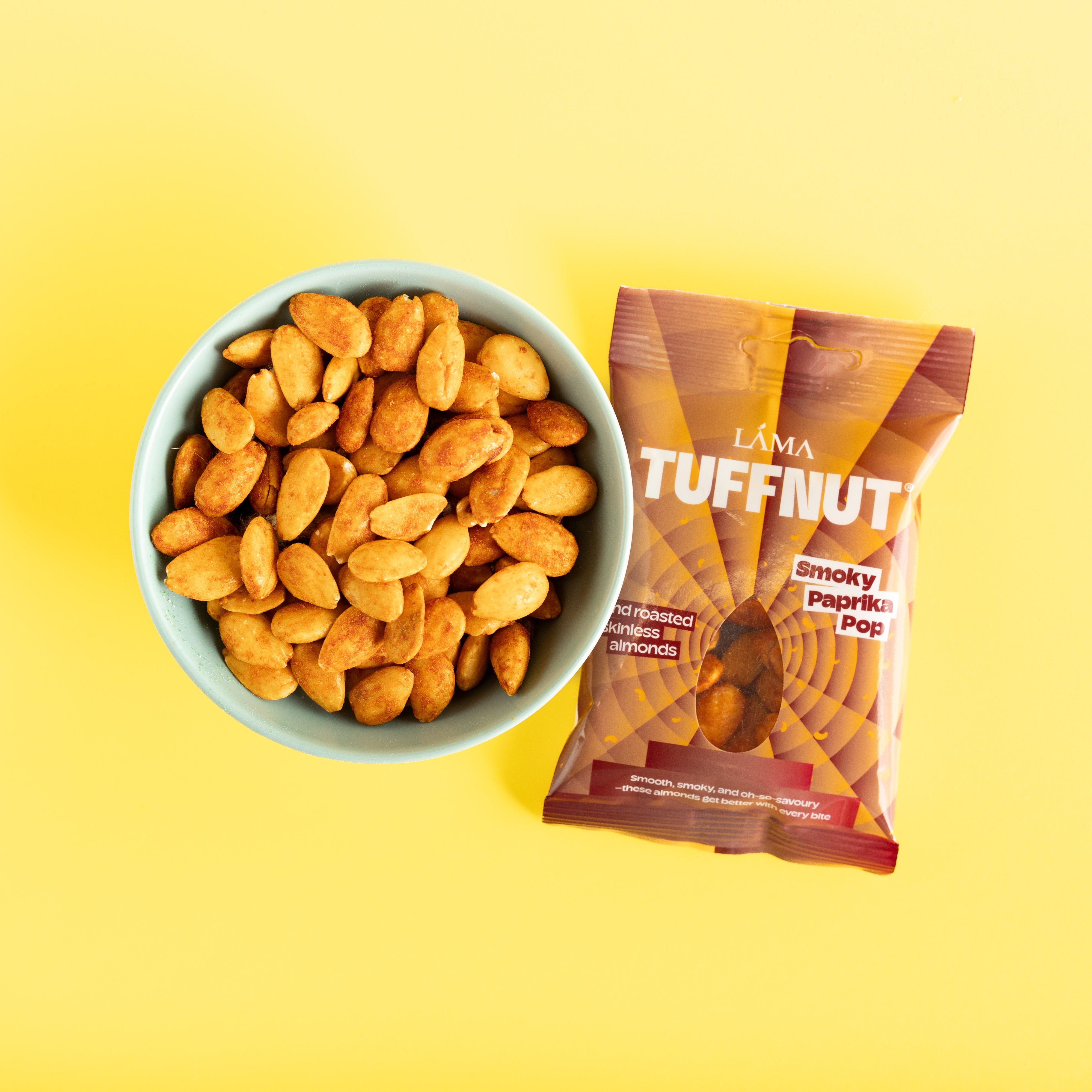 Bowl of roasted Paprika almonds next to a package of Lama Tuffnut on a yellow background
